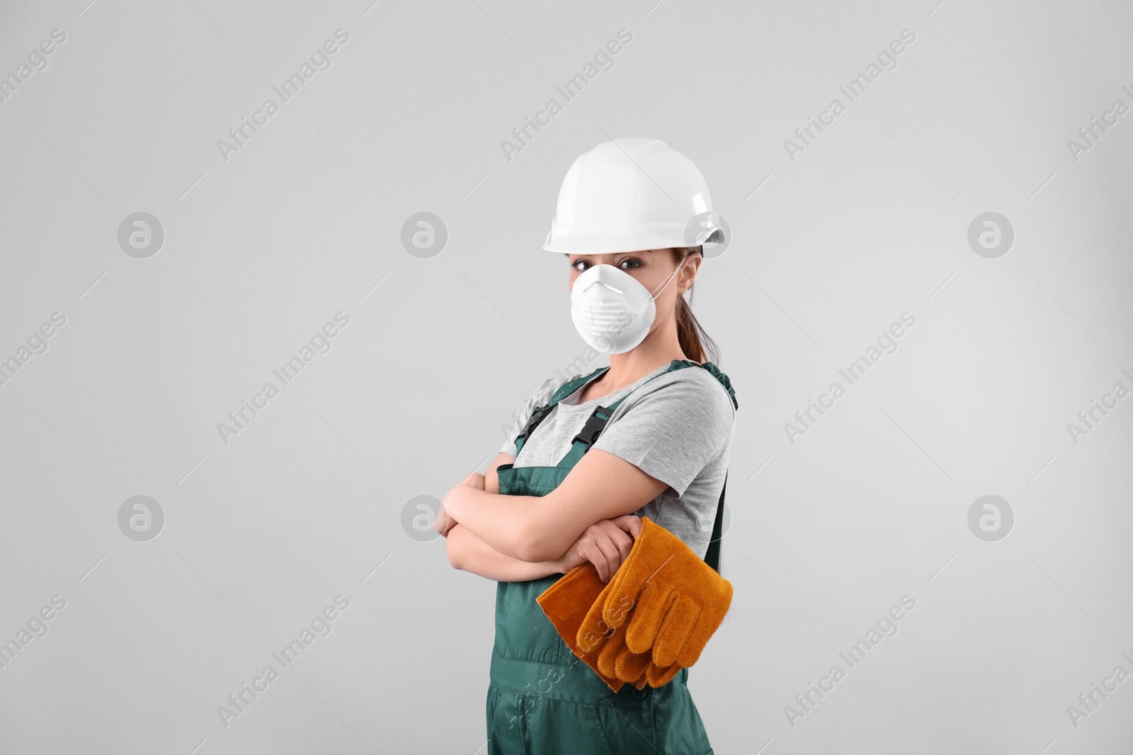 Photo of Female industrial worker in uniform on light background. Safety equipment