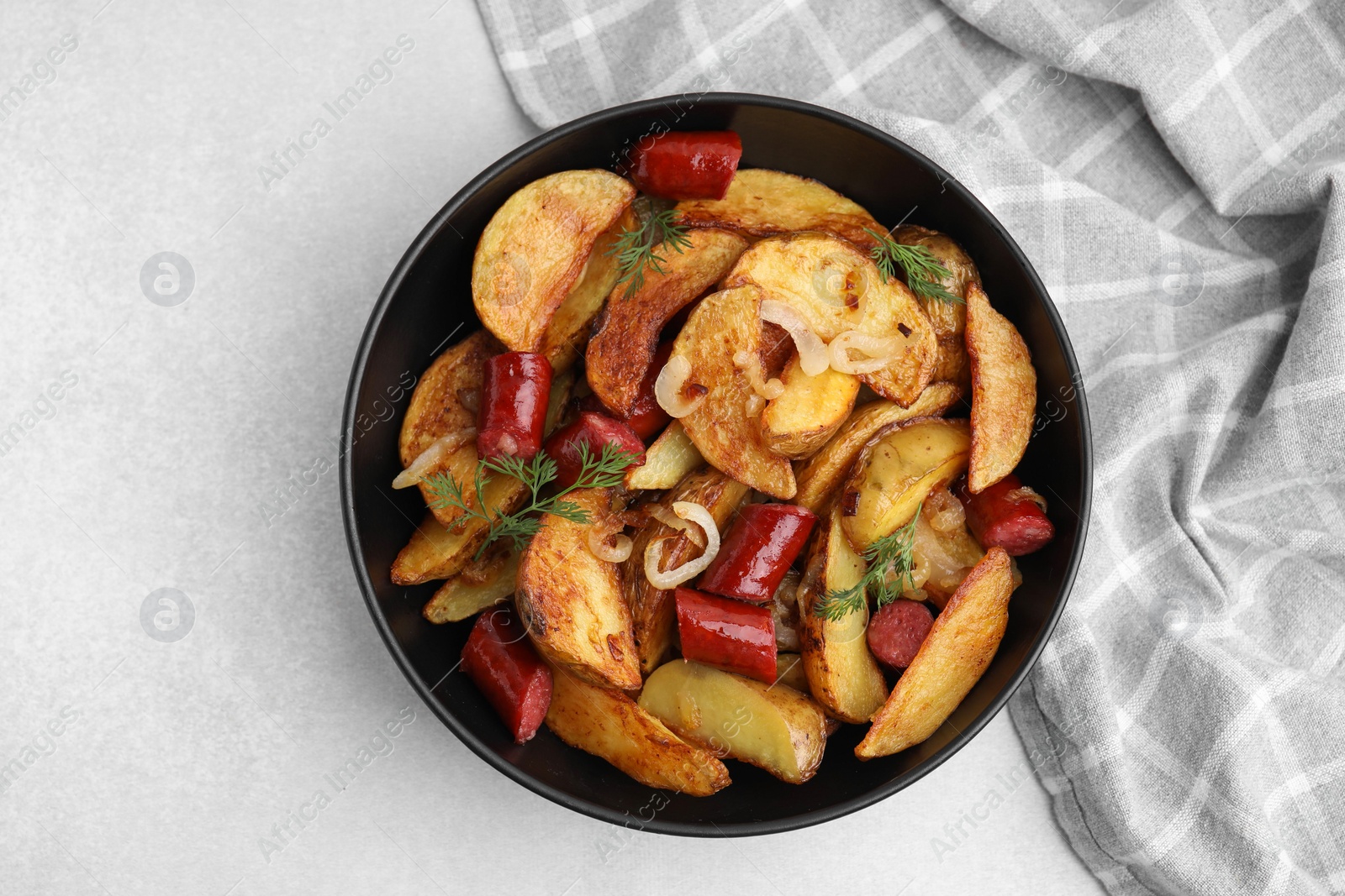 Photo of Delicious baked potato with thin dry smoked sausages, onion and dill in bowl on gray table, top view