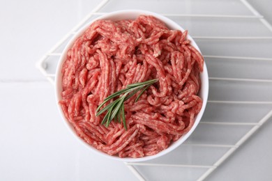 Fresh raw ground meat and rosemary in bowl on white tiled table, top view