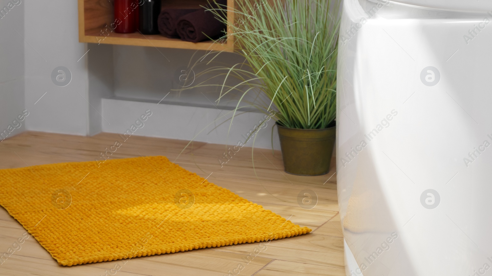 Photo of Soft bath mat near tub and houseplant on wooden floor in bathroom