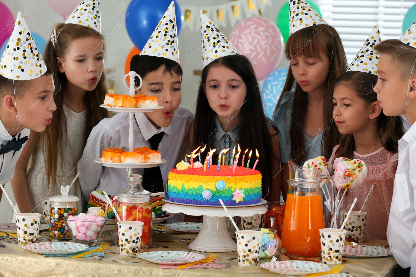 Photo of Happy children blowing out candles on cake at birthday party indoors