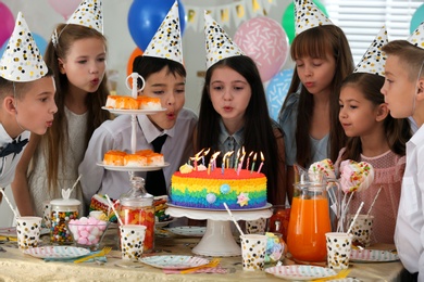 Photo of Happy children blowing out candles on cake at birthday party indoors