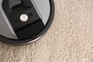 Modern robotic vacuum cleaner on beige carpet, closeup. Space for text