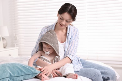 Mother wrapping her cute little baby with towel after bathing on bed