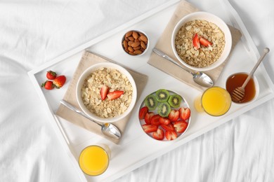 Photo of Tasty breakfast served in bed. Oatmeal, juice, fruits, almonds and honey on tray, top view