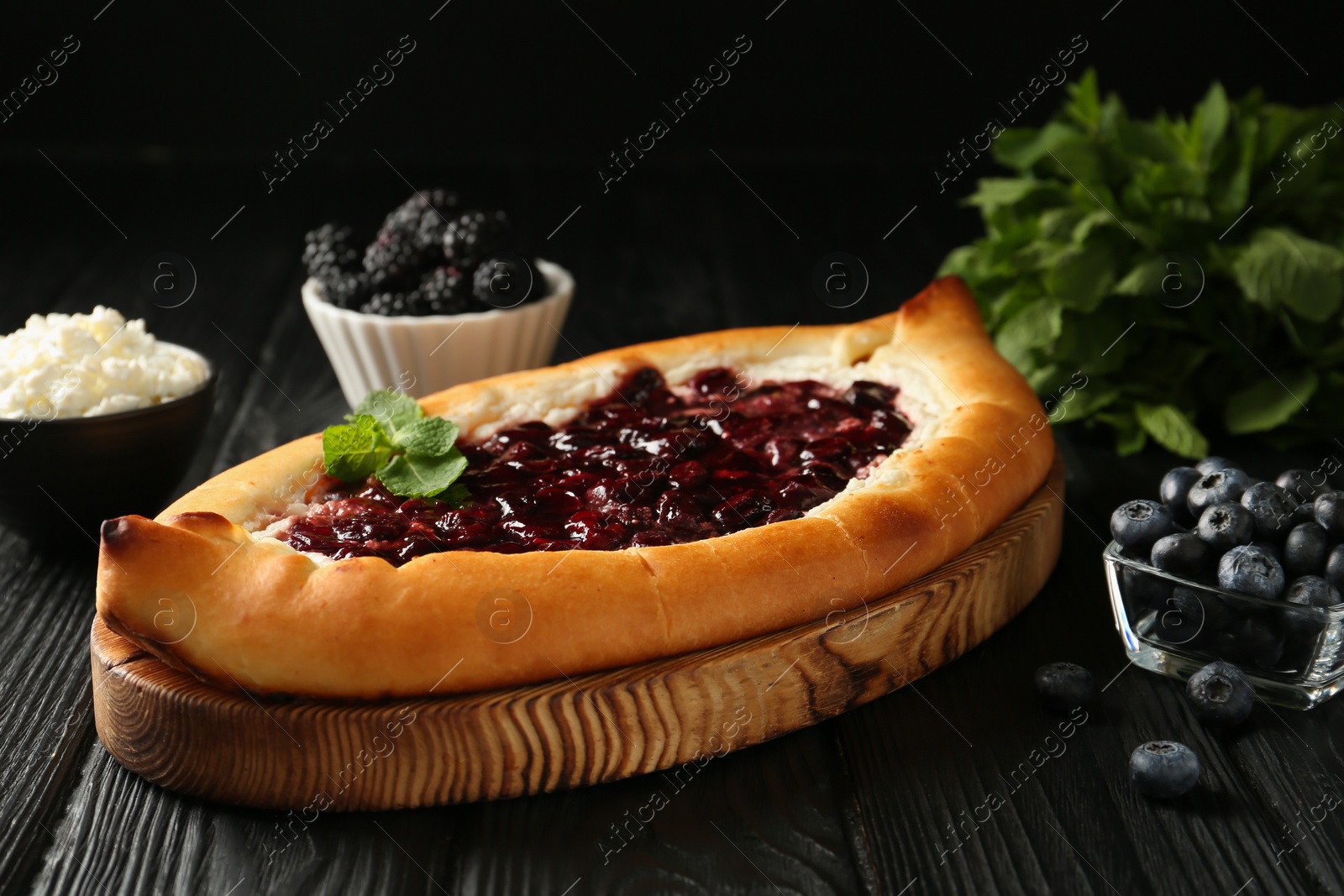 Photo of Delicious sweet cottage cheese pastry with cherry jam on black wooden table