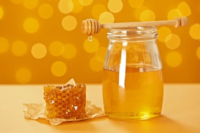 Photo of Jar with honey and fresh comb on table against blurred background