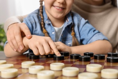 Photo of Playing checkers. Mother learning her daughter at table in room, closeup