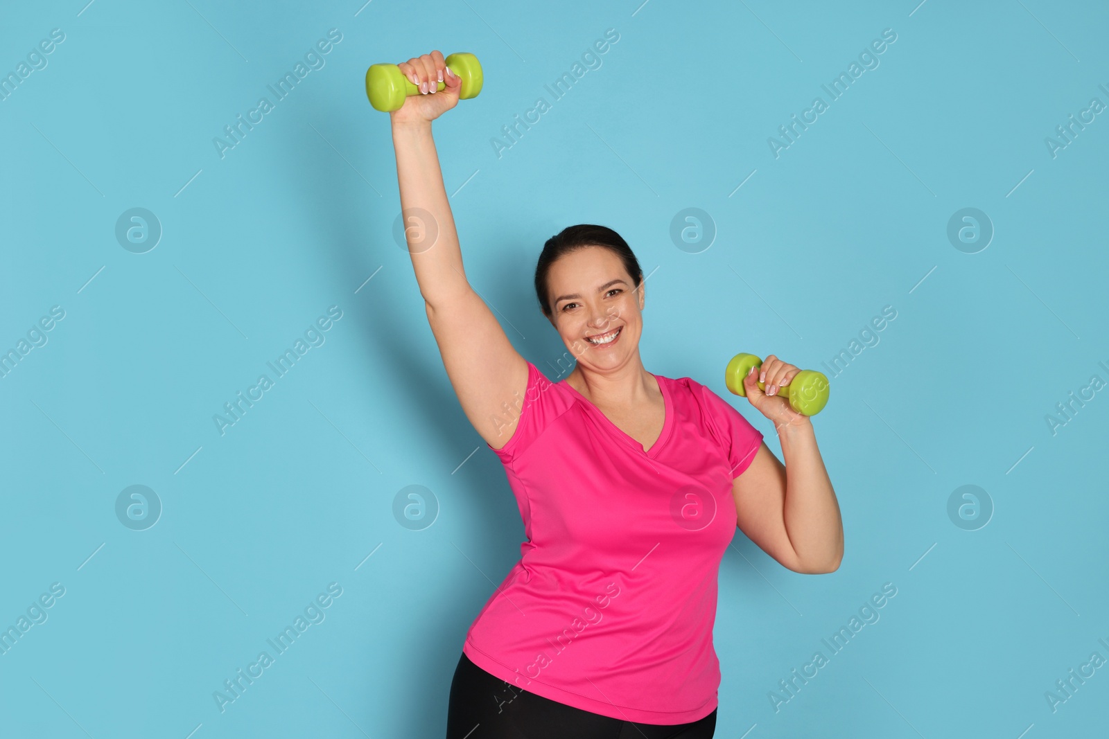 Photo of Happy overweight woman doing exercise with dumbbells on light blue background