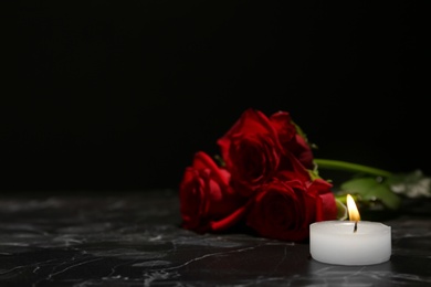 Photo of Beautiful red roses and candle on table against black background. Funeral symbol