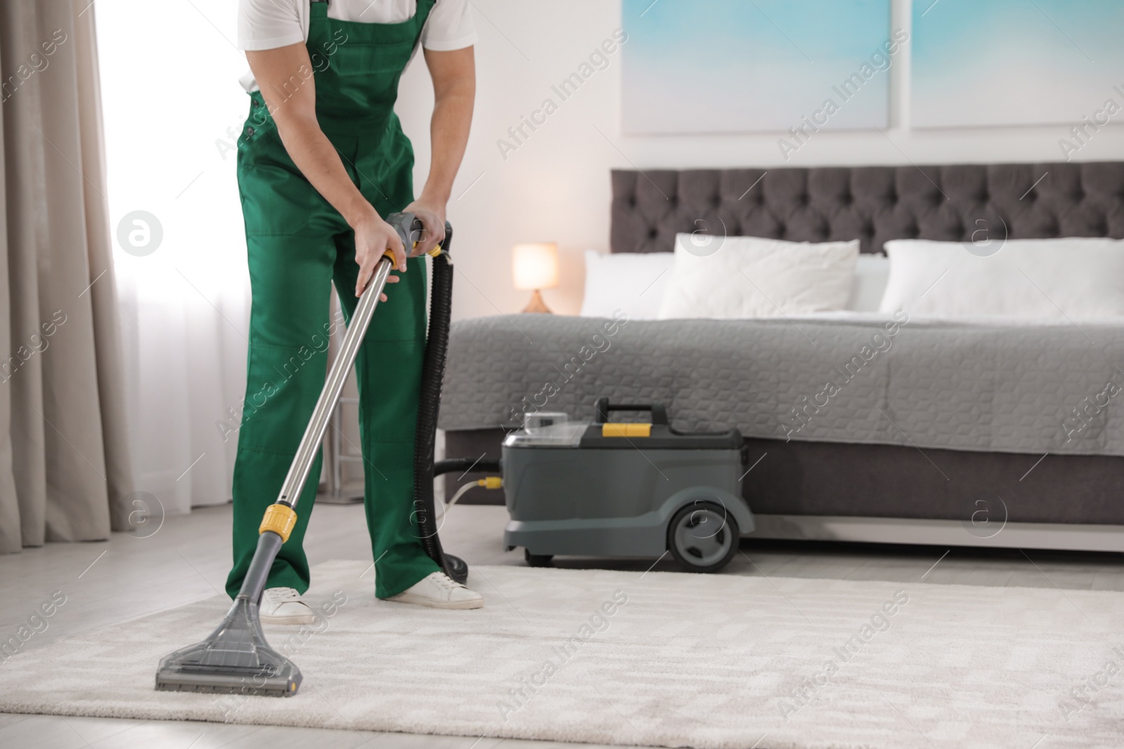 Photo of Professional janitor removing dirt from carpet with vacuum cleaner in bedroom, closeup. Space for text