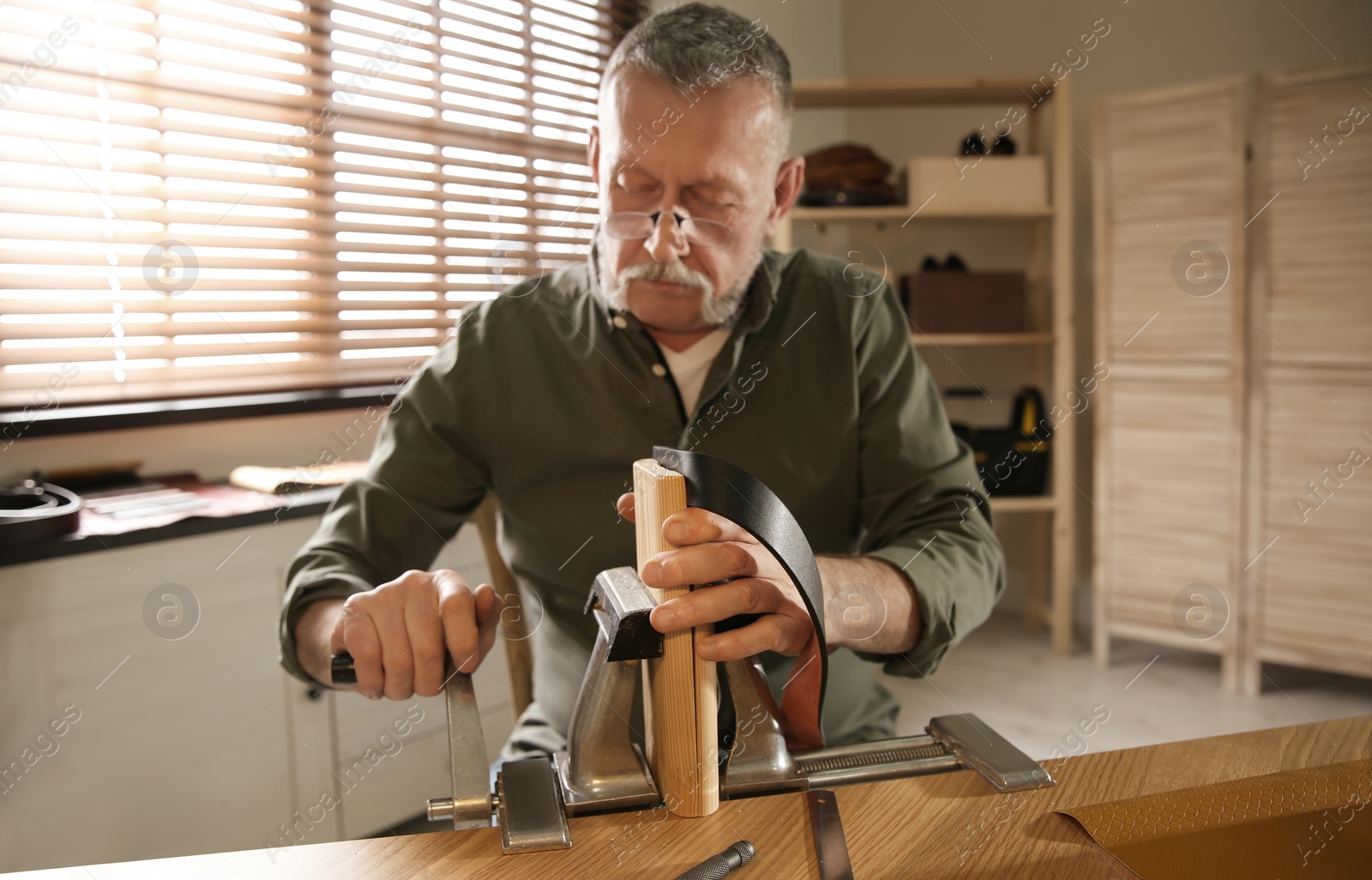 Photo of Man working with leather belt at table in atelier
