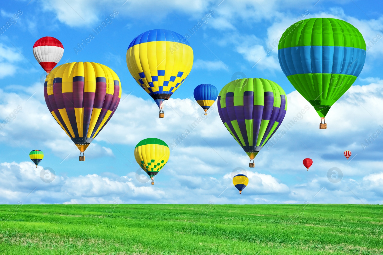 Image of Bright hot air balloons flying in sky with clouds over green meadow