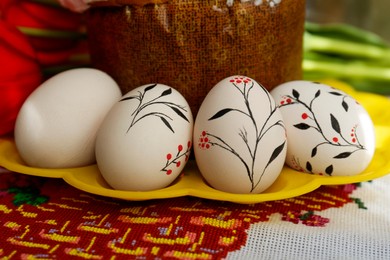 Photo of Eggs with floral ornaments and kulich for Easter on table, closeup