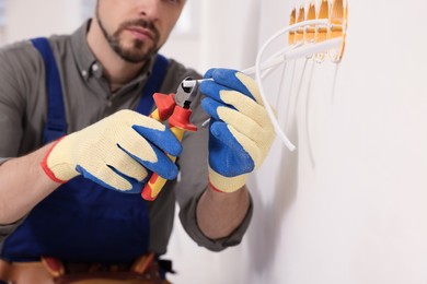 Electrician with pliers repairing power socket indoors, closeup