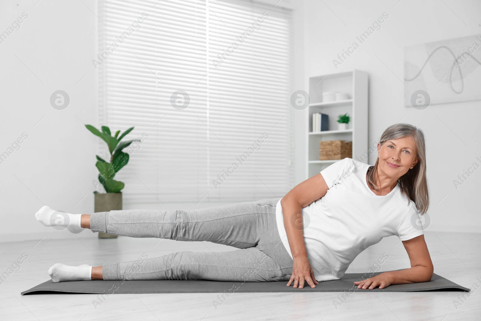 Photo of Happy senior woman practicing yoga on mat at home