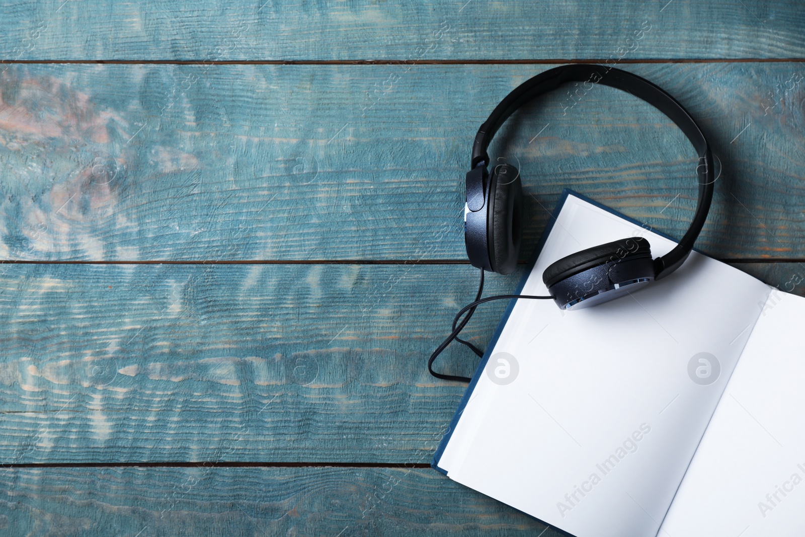 Photo of Modern headphones with hardcover book on wooden background, top view. Space for text