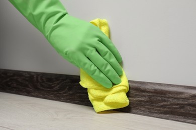 Photo of Woman in gloves cleaning plinth with cloth indoors, closeup