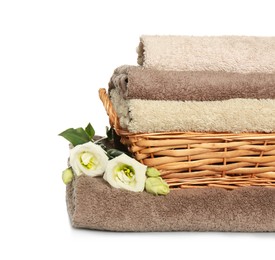 Photo of Wicker basket with folded soft terry towels and flowers on white background