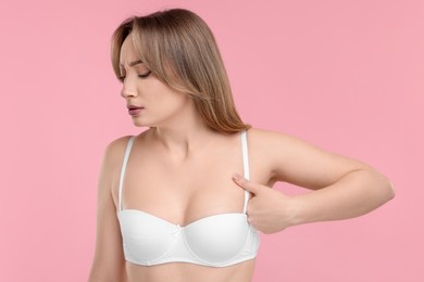 Mammology. Young woman doing breast self-examination on pink background