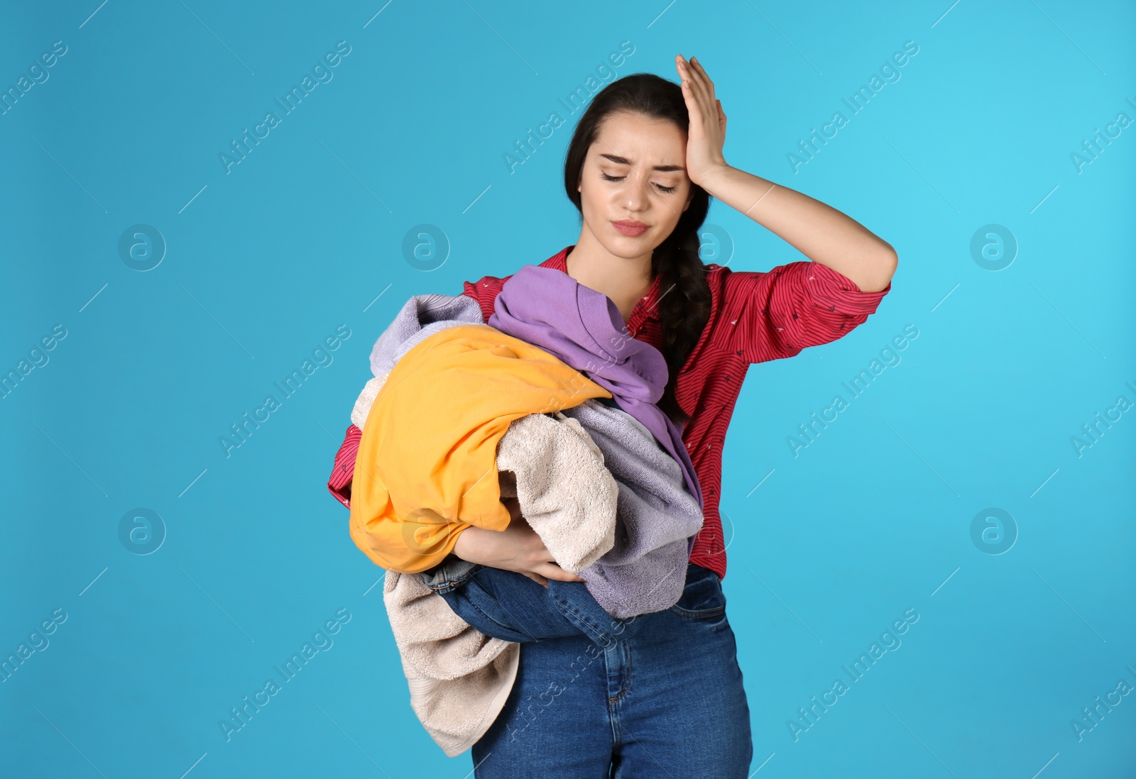 Photo of Displeased young woman holding pile of dirty laundry on color background