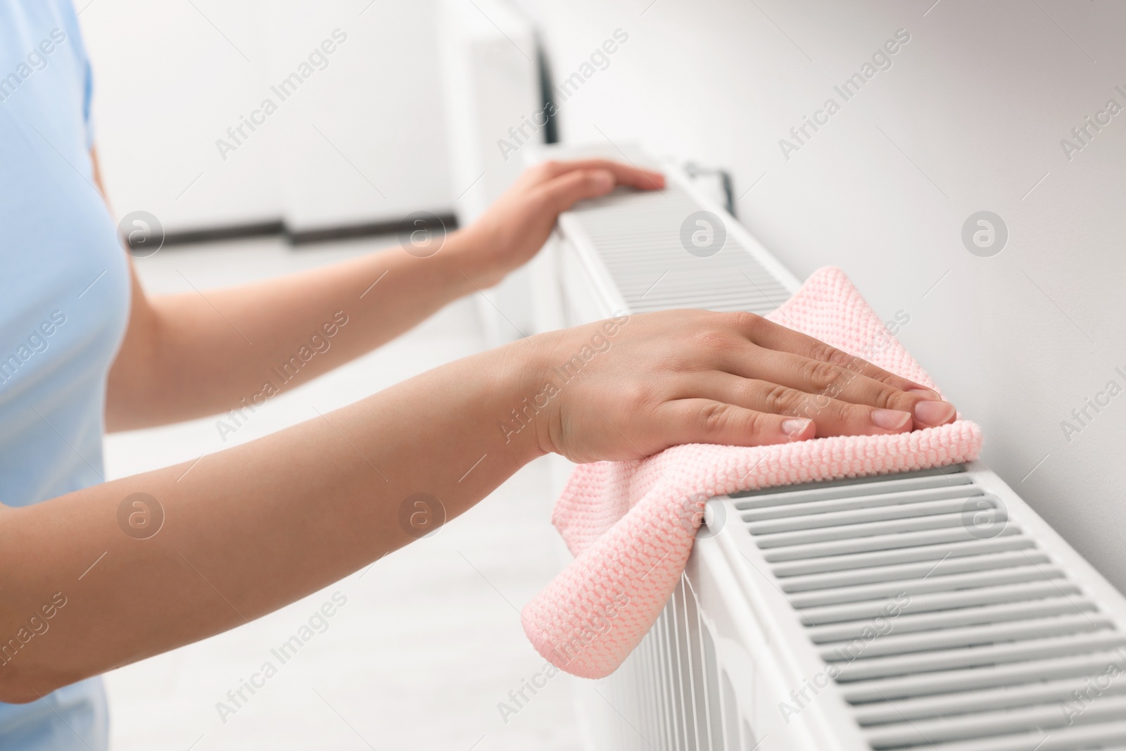 Photo of Woman cleaning radiator with rag indoors, closeup