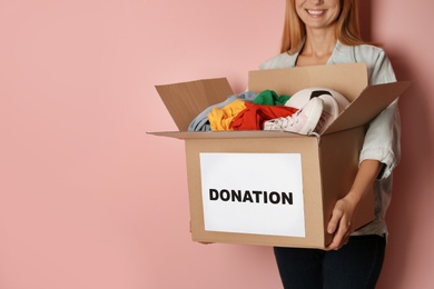Woman holding box with donations on color background. Space for text