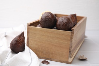 Photo of Wooden crate with fresh salak fruits on white table, closeup