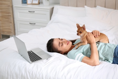 Photo of Young woman with chihuahua and laptop on bed. Home office concept