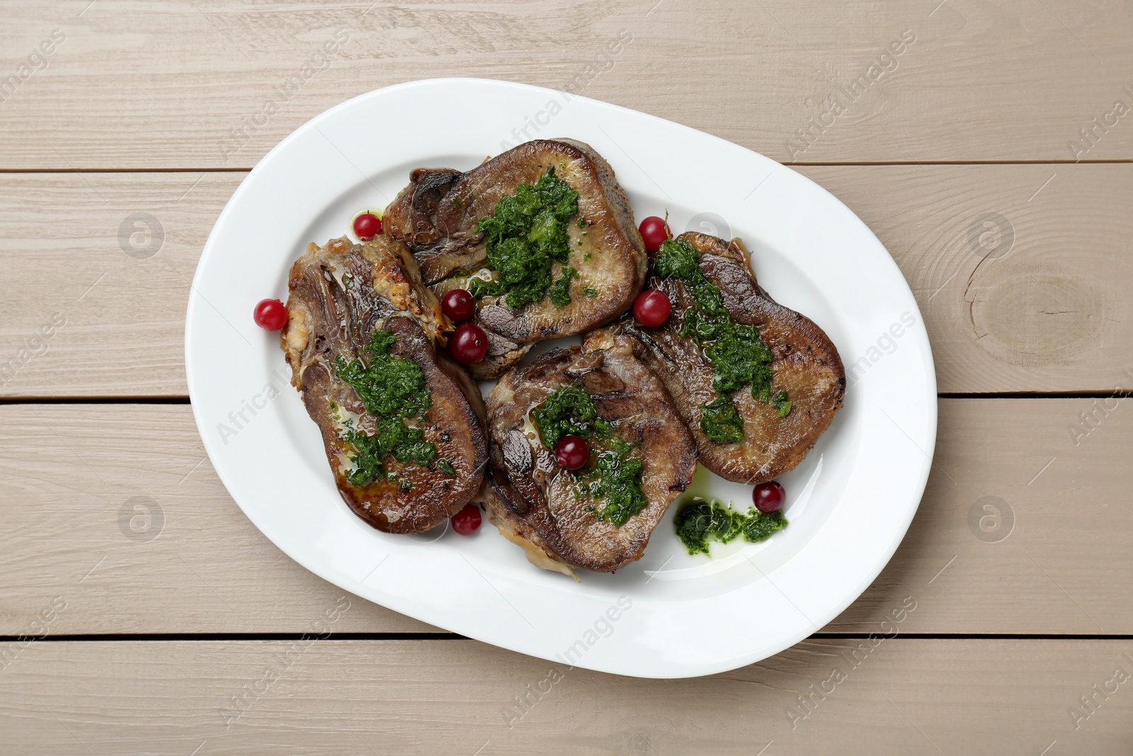 Photo of Tasty beef tongue pieces, salsa verde and berries on beige wooden table, top view