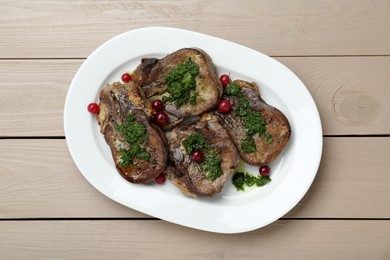 Tasty beef tongue pieces, salsa verde and berries on beige wooden table, top view