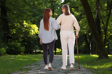 Photo of Senior lady with walking cane and young woman in park, back view