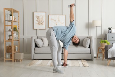 Photo of Overweight man doing exercise with dumbbells at home