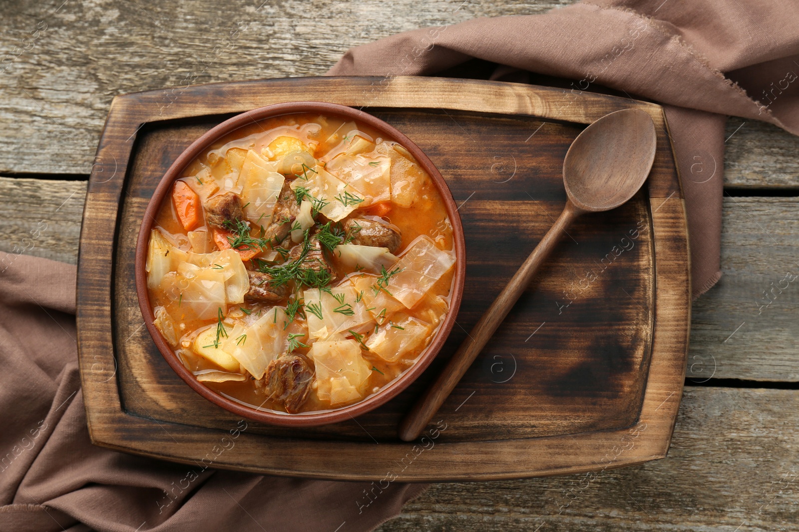 Photo of Tasty cabbage soup with meat, carrot and dill on wooden table, top view