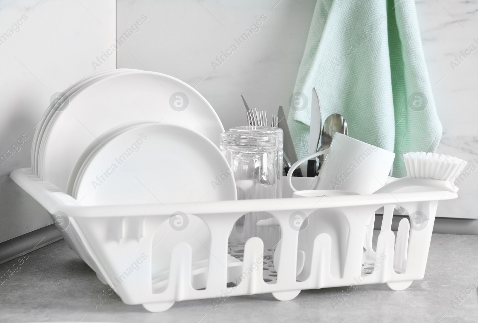 Photo of Drying rack with clean dishes and cutlery on table near light wall