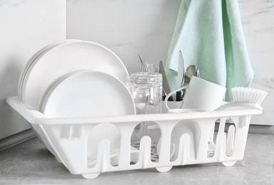 Drying rack with clean dishes and cutlery on table near light wall