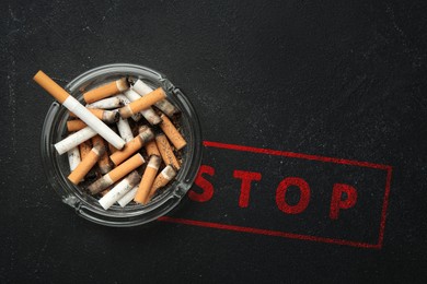 Image of Quit smoking. Glass ashtray with stubs and word Stop on black table, top view