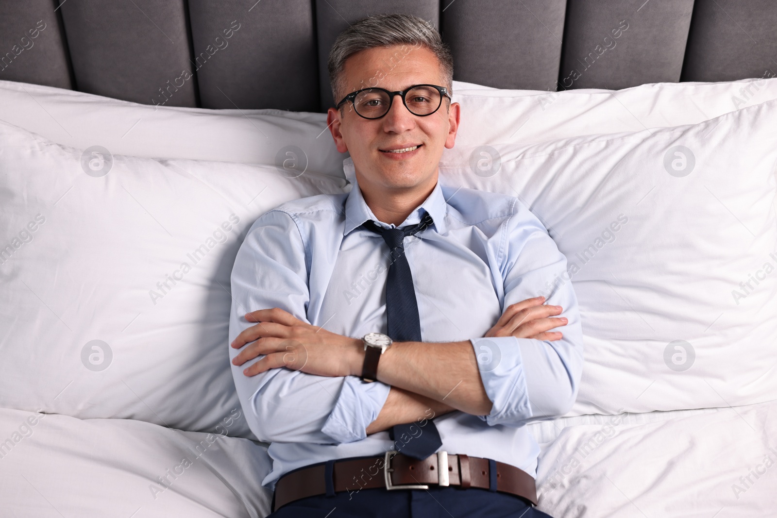 Photo of Businessman in glasses lying on bed indoors, above view