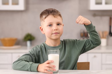 Photo of Cute boy with glassfresh milk showing his strength at white table in kitchen