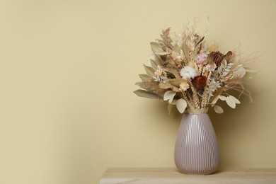 Photo of Beautiful dried flower bouquet in ceramic vase on wooden table near beige wall. Space for text