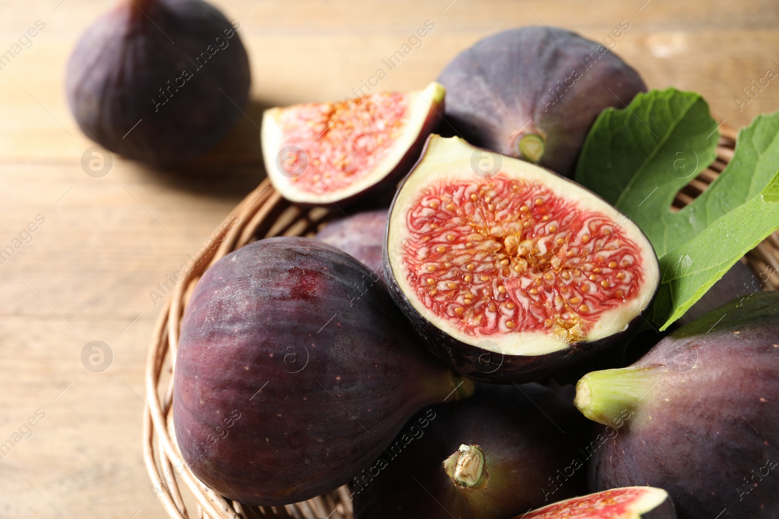 Photo of Wicker bowl with fresh ripe figs and green leaf on wooden table, closeup