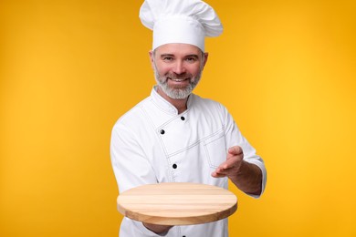 Photo of Happy chef in uniform with wooden board on orange background