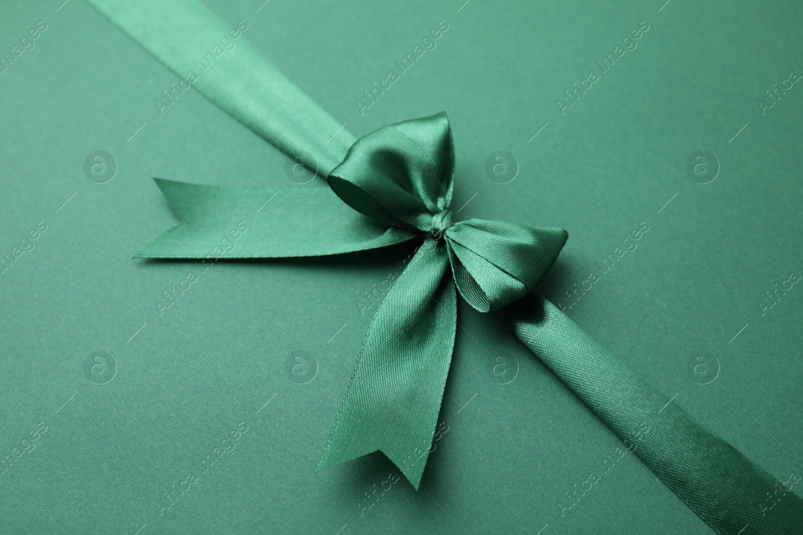 Photo of Bright satin ribbon with bow on green background