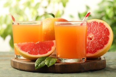 Photo of Glasses of delicious grapefruit juice on wooden table against blurred background