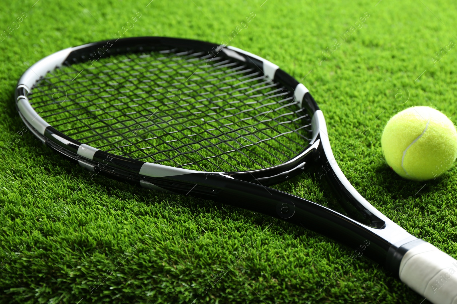 Photo of Tennis racket and ball on green grass, closeup. Sports equipment