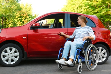 Photo of Young woman in wheelchair opening door of car outdoors