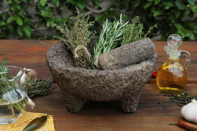 Mortar, different herbs, vegetables and oil on wooden table outdoors