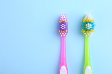 Colorful plastic toothbrushes on light blue background, flat lay. Space for text
