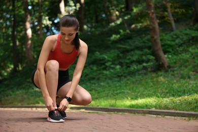 Photo of Beautiful woman in sportswear tying shoelaces in park. Space for text