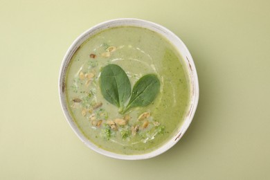Photo of Delicious broccoli cream soup with basil and pumpkin seeds on green background, top view